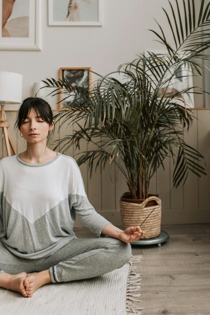Adult woman meditating indoors with incense, creating a calm and relaxing atmosphere.